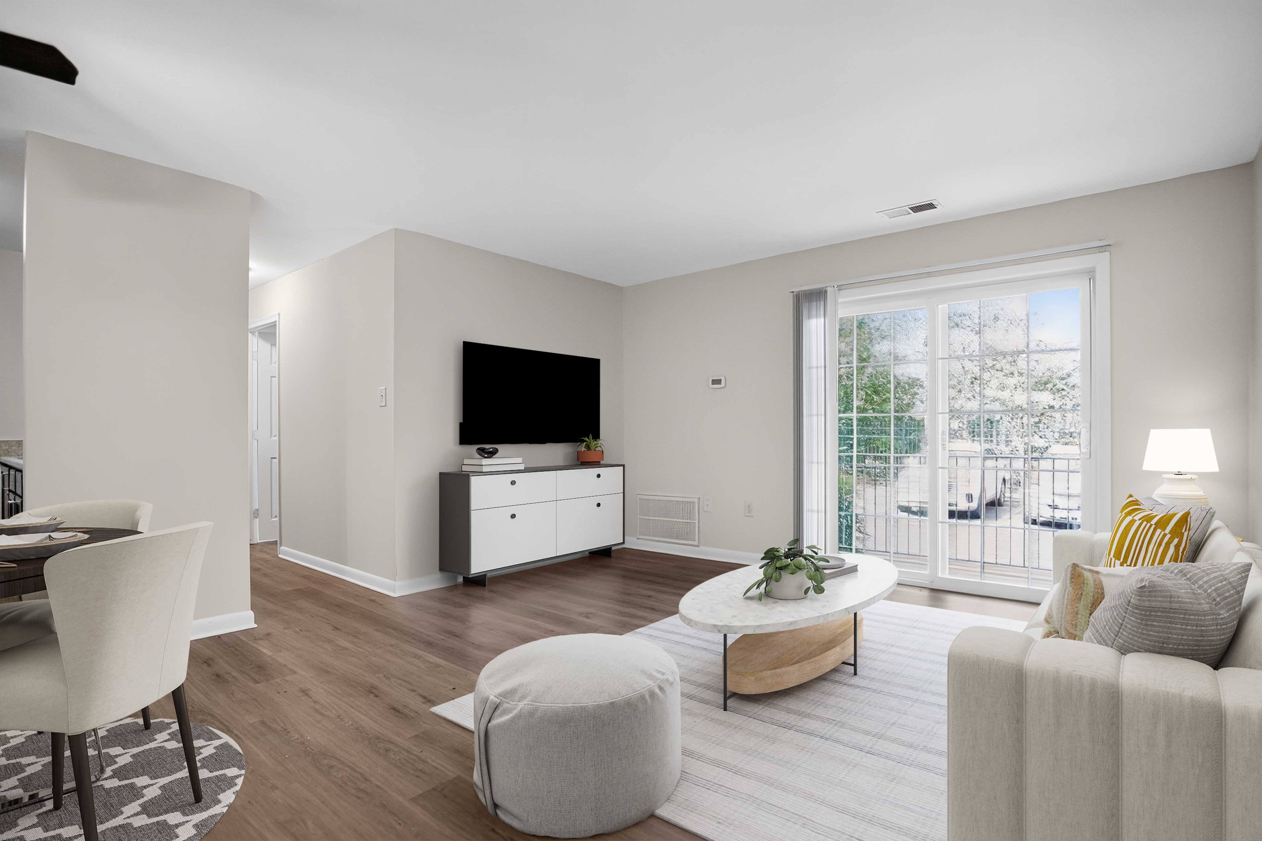 A living room with a grey couch, a white chair, a white ottoman, a wooden coffee table, a flat screen TV, and a sliding glass door.